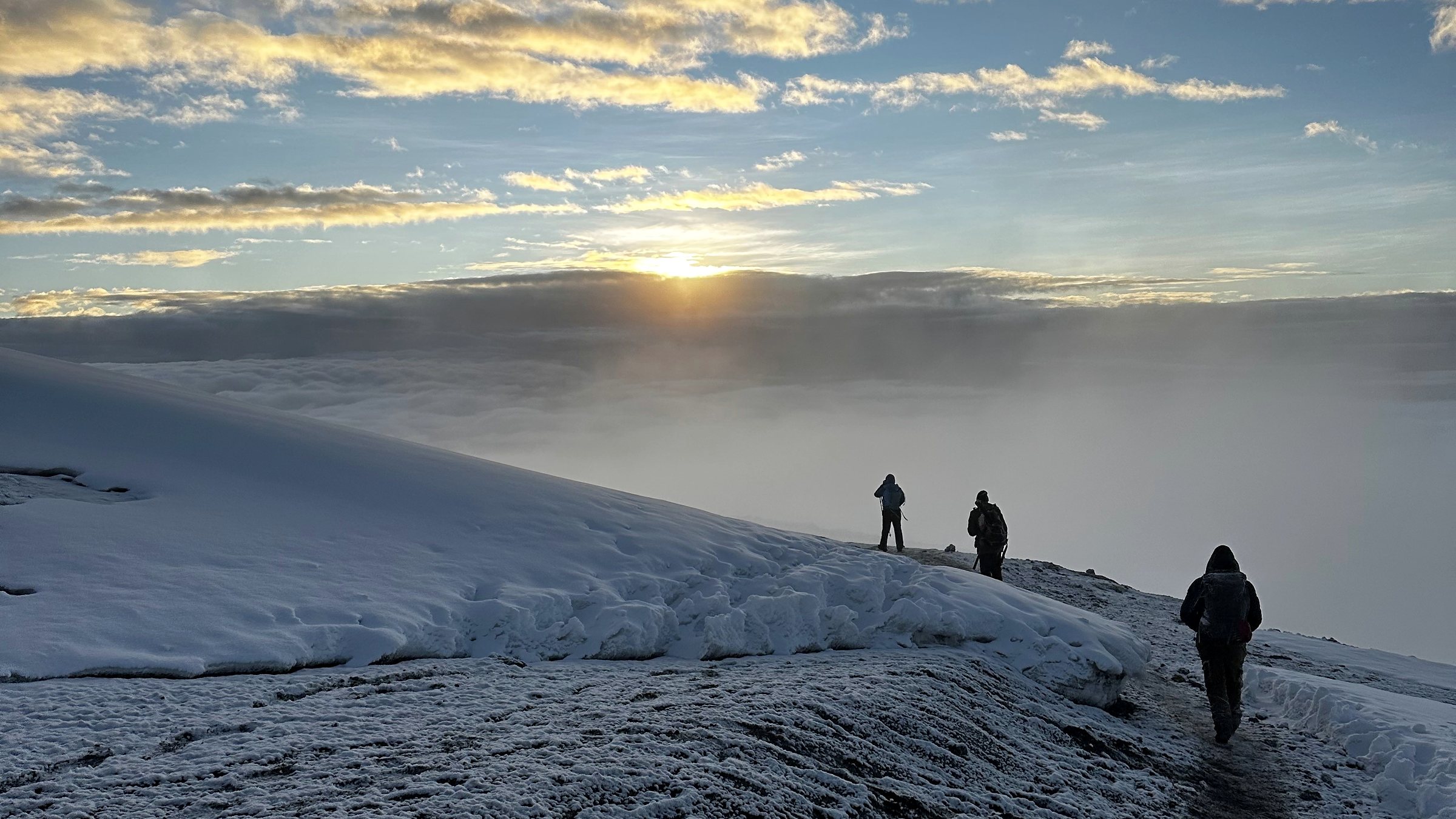 Ascension du Kilimandjaro au lever du jour : silhouettes de marcheurs sur la crête, au-dessus de la mer de nuages
